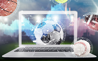 An open laptop and different sports balls representing sports betting